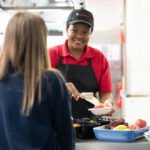 Solihull Catering staff member serving a student lunch from the counter.