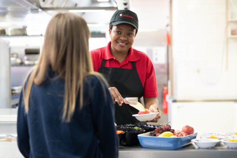 Solihull Catering staff member serving a student lunch from the counter.